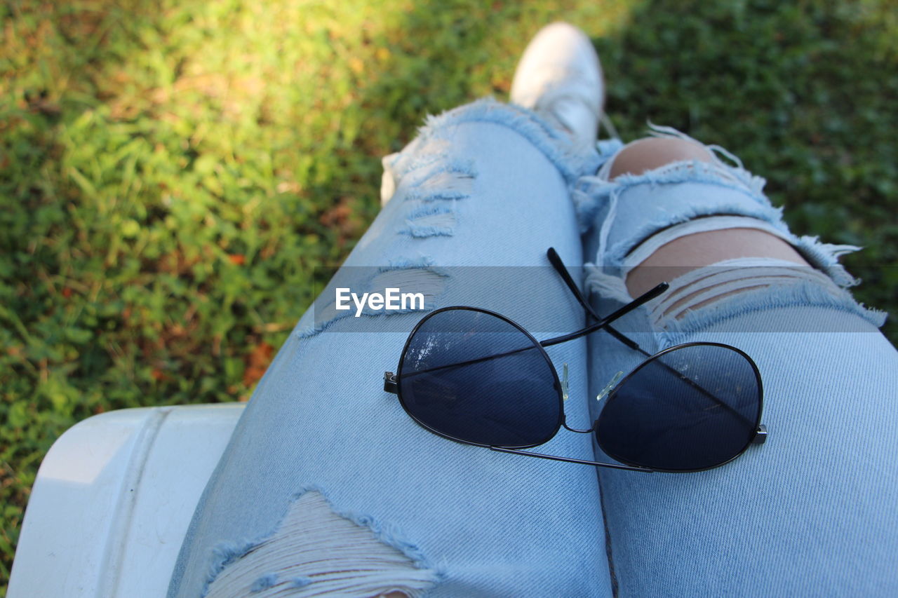 High angle view of sunglasses on lap of woman wearing torn jeans