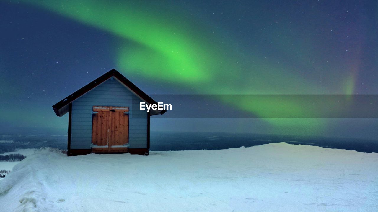 House on snow landscape against northern lights