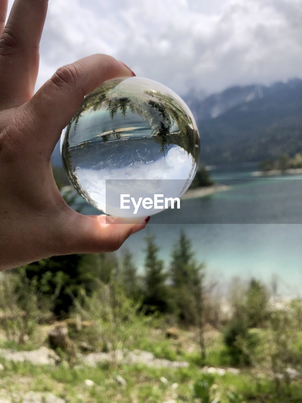 Cropped hand holding crystal ball against sky