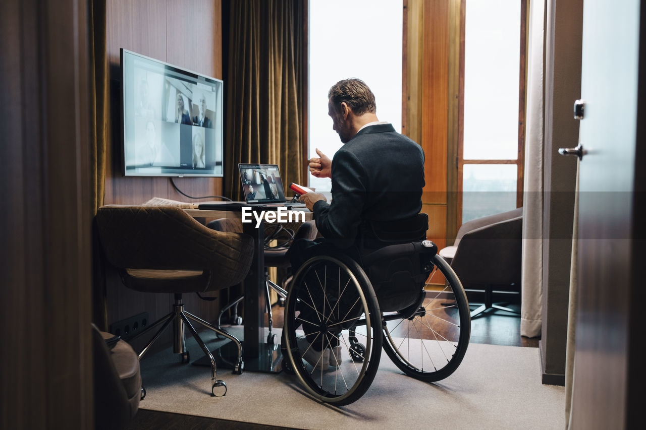 Disabled businessman with colleagues on video conference in office during pandemic