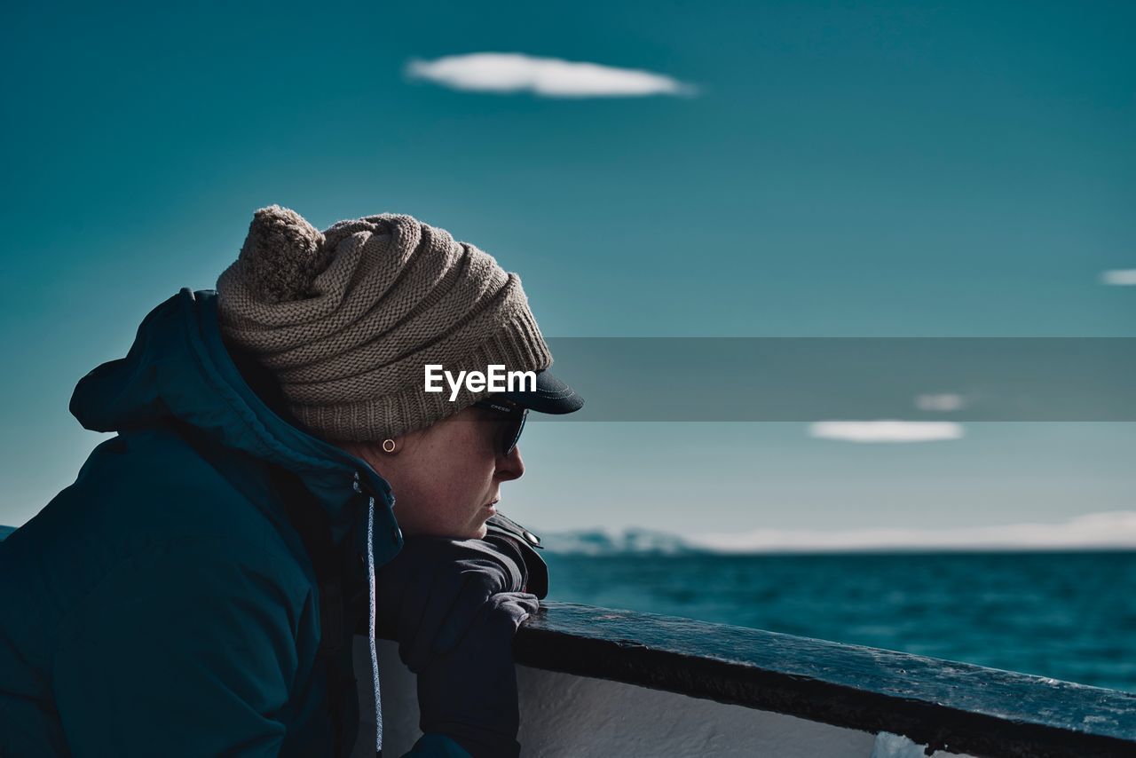 Side view of woman wearing hat on railing of boat on sea against blue sky