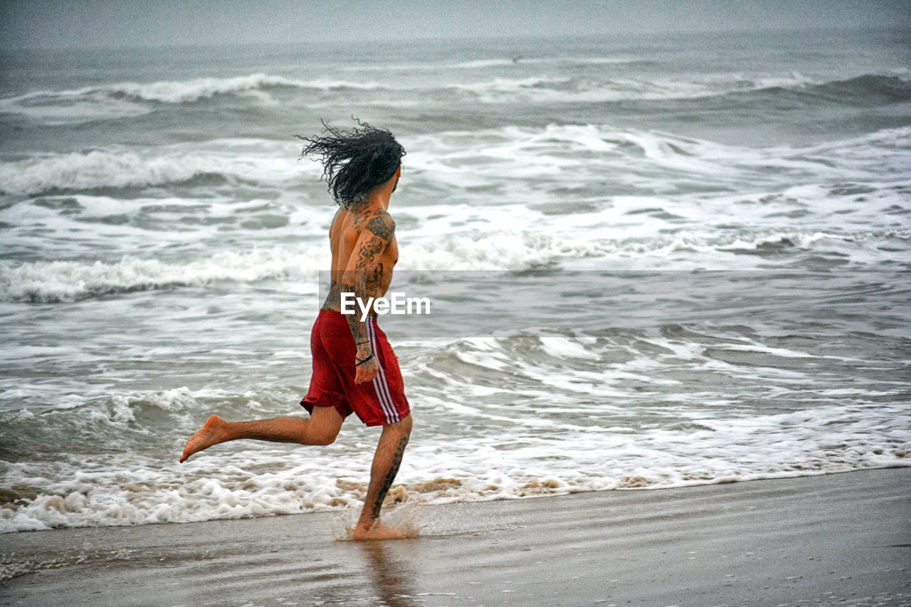 Shirtless man running at sea shore