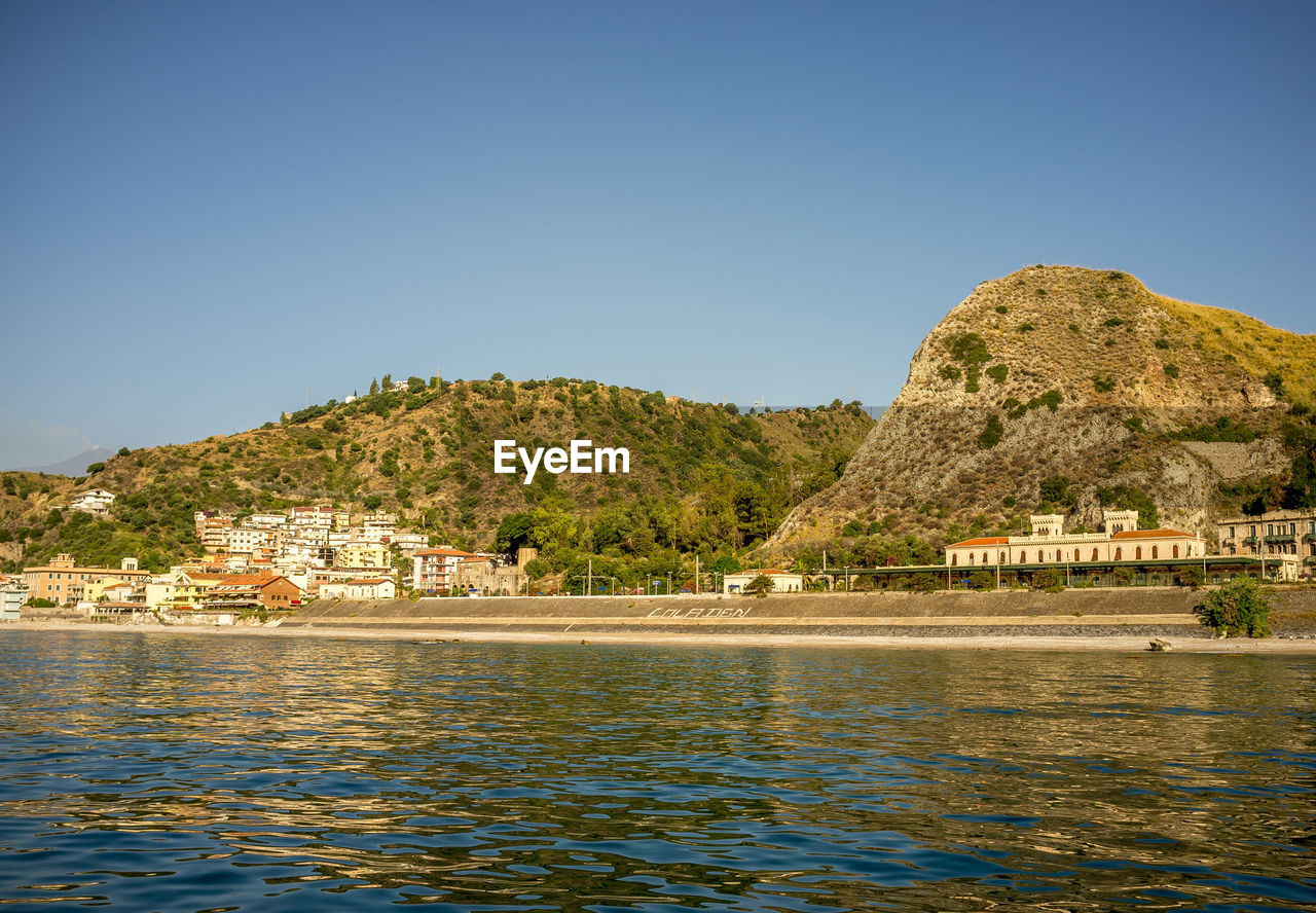 Scenic view of sea by buildings against clear blue sky