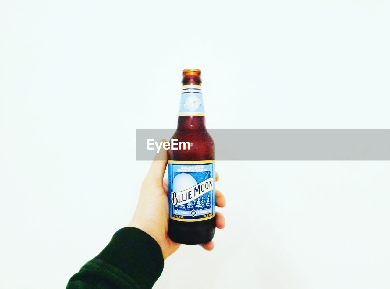 CLOSE-UP OF HAND HOLDING DRINK BOTTLE AGAINST WHITE BACKGROUND