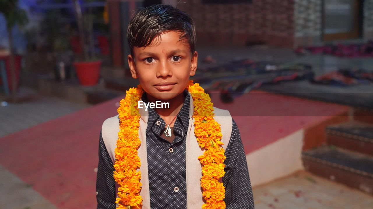 Cute and innocent asian boy with yellow flowers garland looking at cameraman.