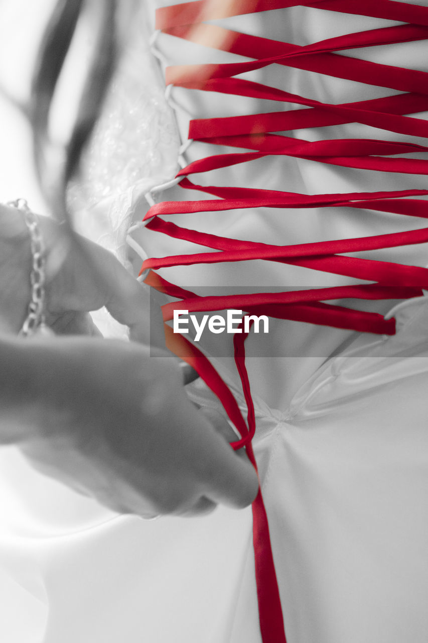 Close-up of hand tying red band on wedding dress