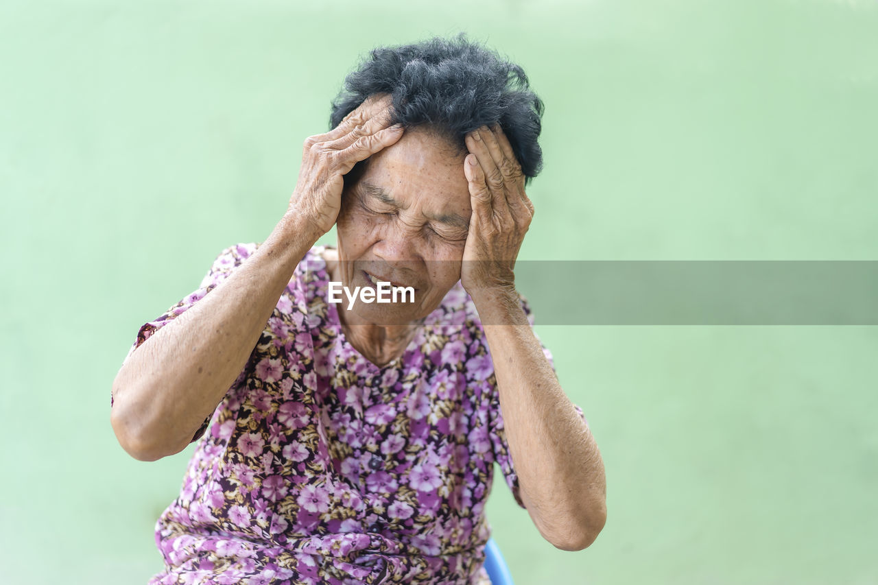 Senior black-haired woman touching head with hand with painful expression because of headache.