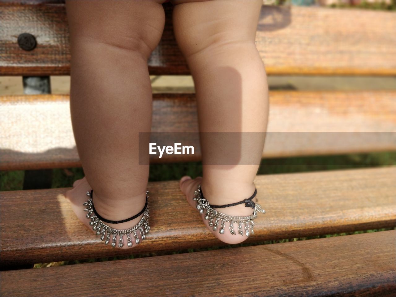 Low section of baby girl wearing anklets standing on bench