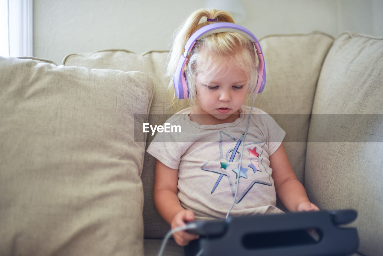 Cute girl using digital tablet while sitting on sofa at home