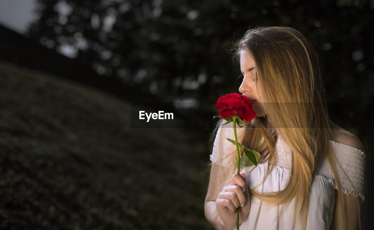 Close-up of woman holding rose against trees