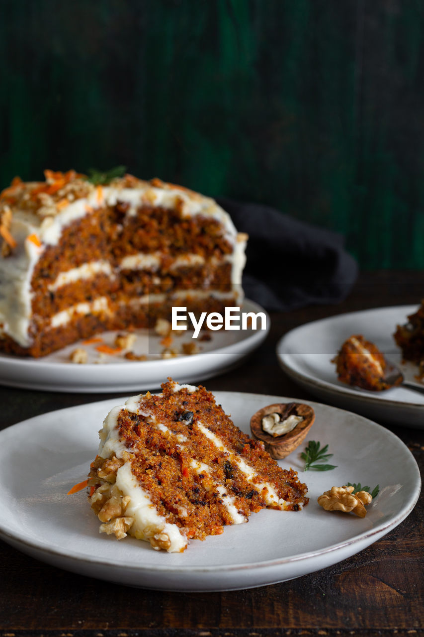 Yummy cake with cream cheese served on plates with fresh carrot slices and walnuts