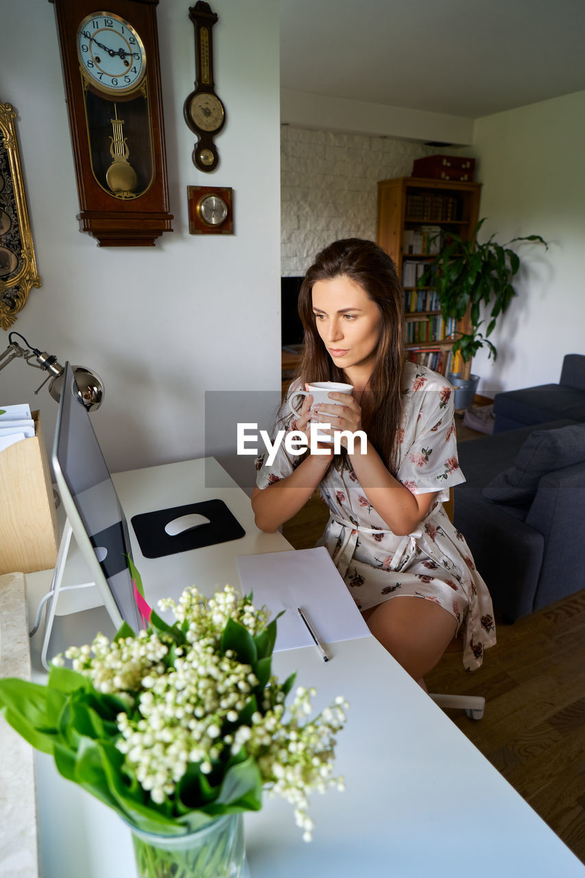 Woman holding coffee mug while looking at computer