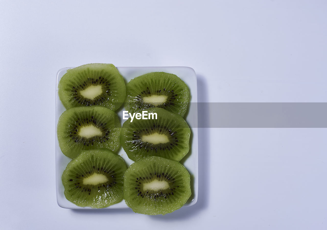 Halved kiwis on a rectangular plate, white and bright background, symmetry, empty space, zenithal