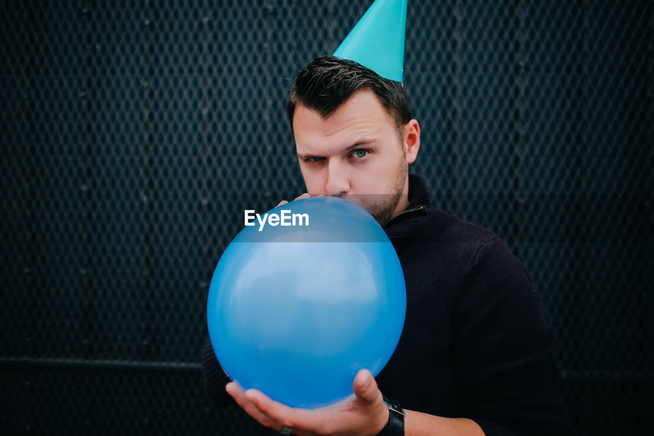 Portrait of man blowing balloon against metal grate