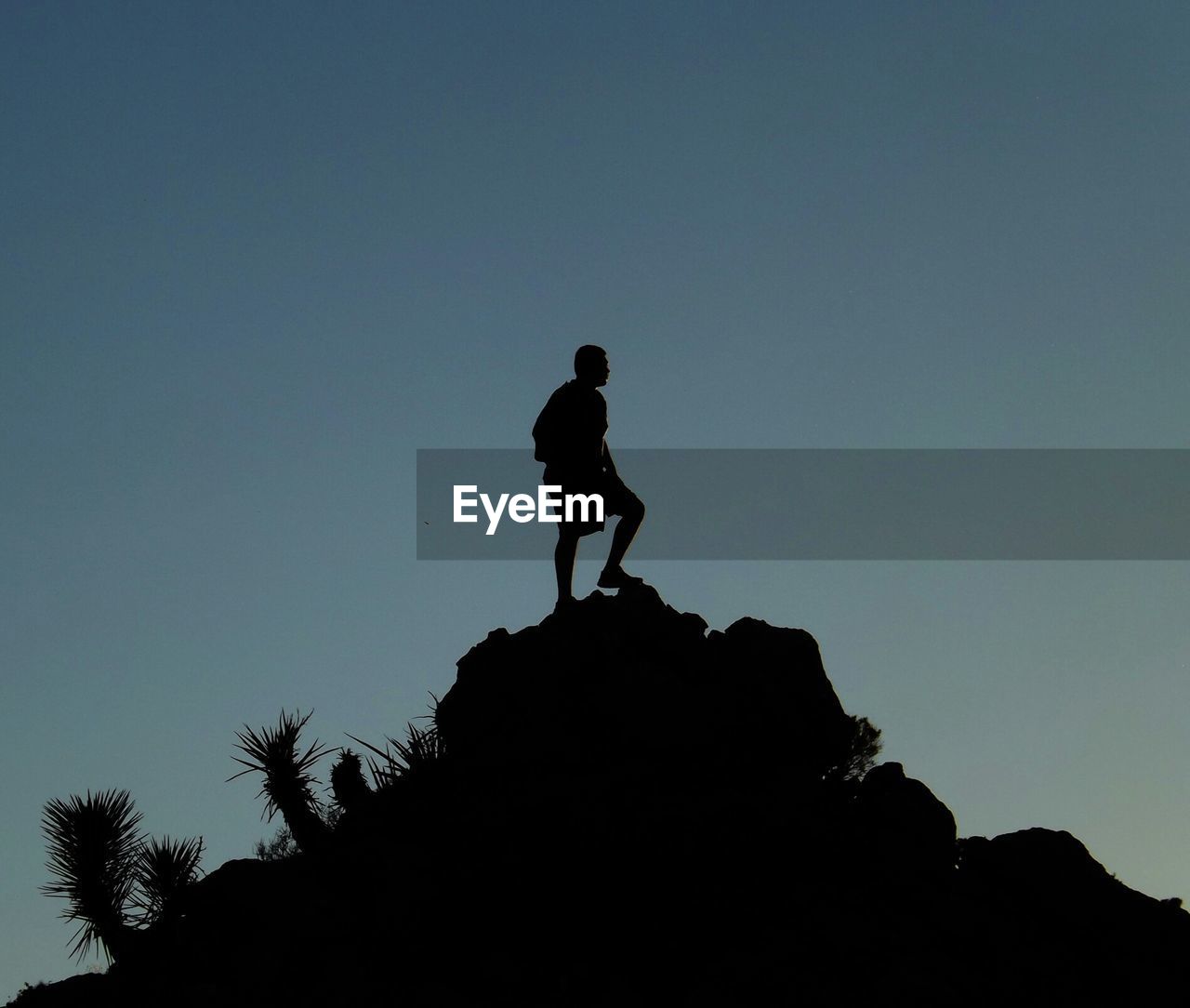 Low angle view of silhouette man standing on rock against clear sky