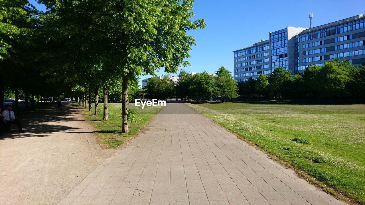 Footpath amidst trees and buildings against sky