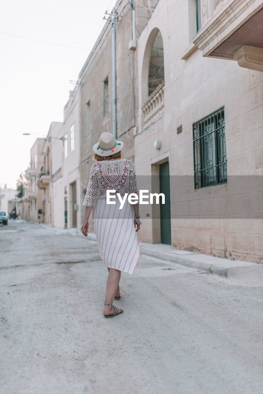 FULL LENGTH REAR VIEW OF WOMAN WALKING ON STREET AGAINST BUILDING