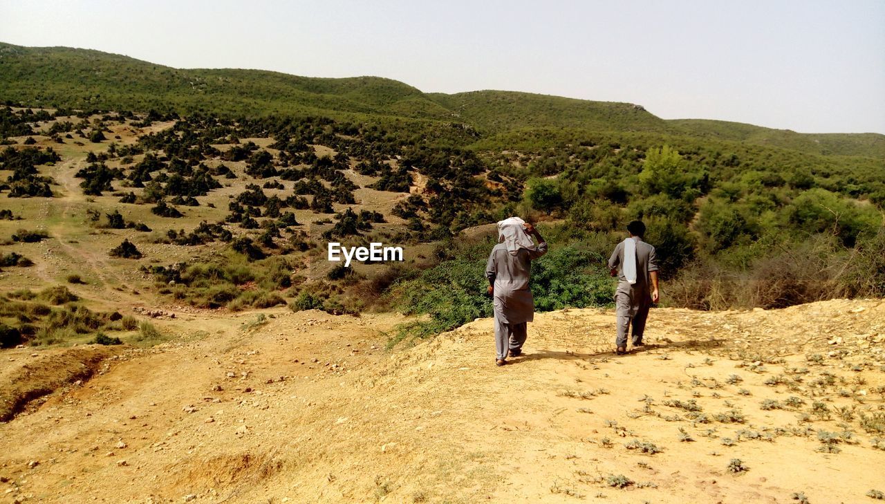 Rear view of men walking on dirt road against sky