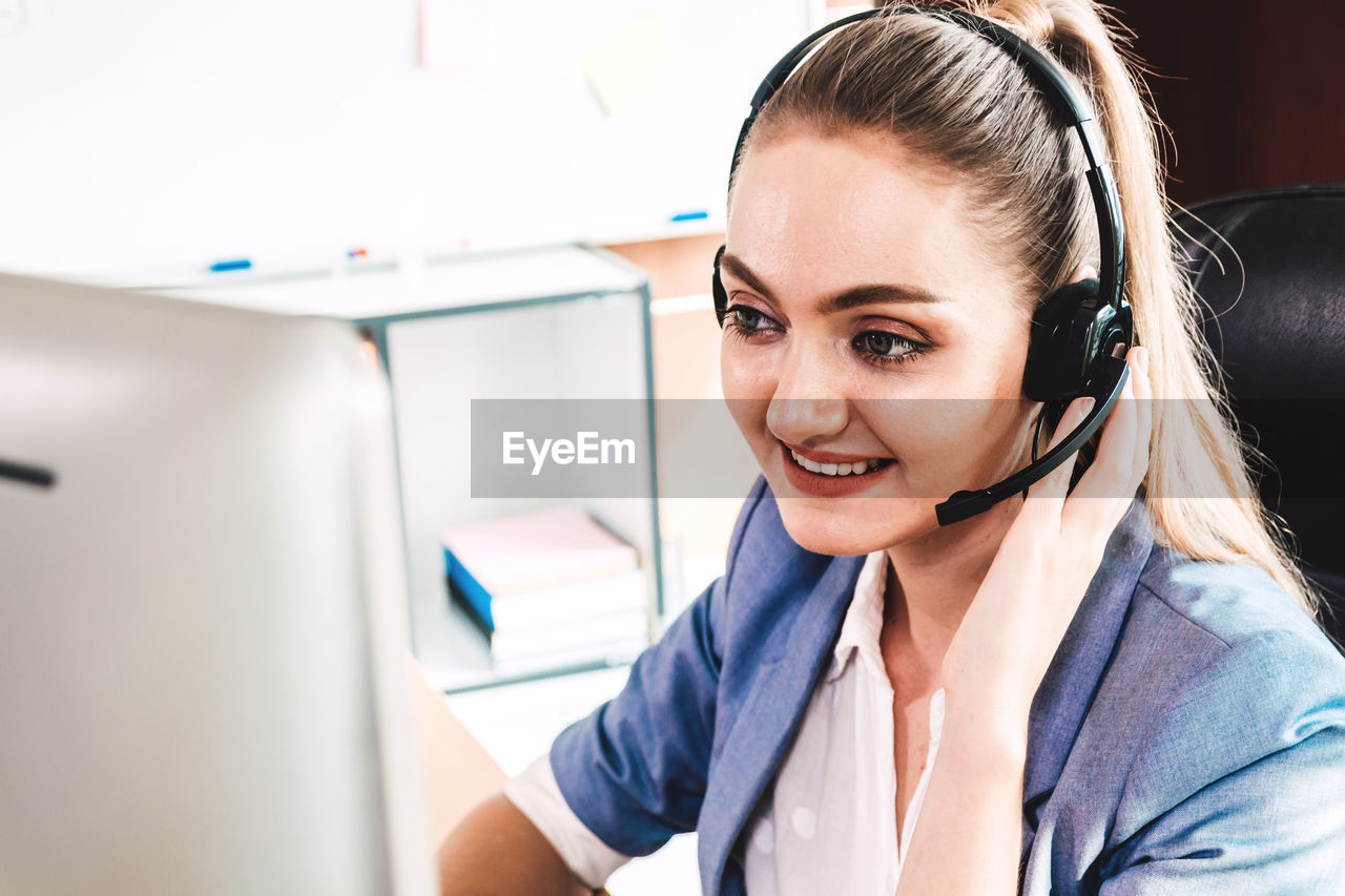 Smiling businesswoman wearing headset looking at computer on desk in office