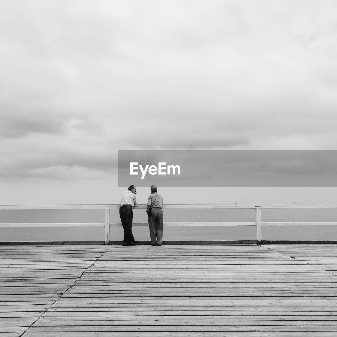 Rear view of friends standing on pier over sea