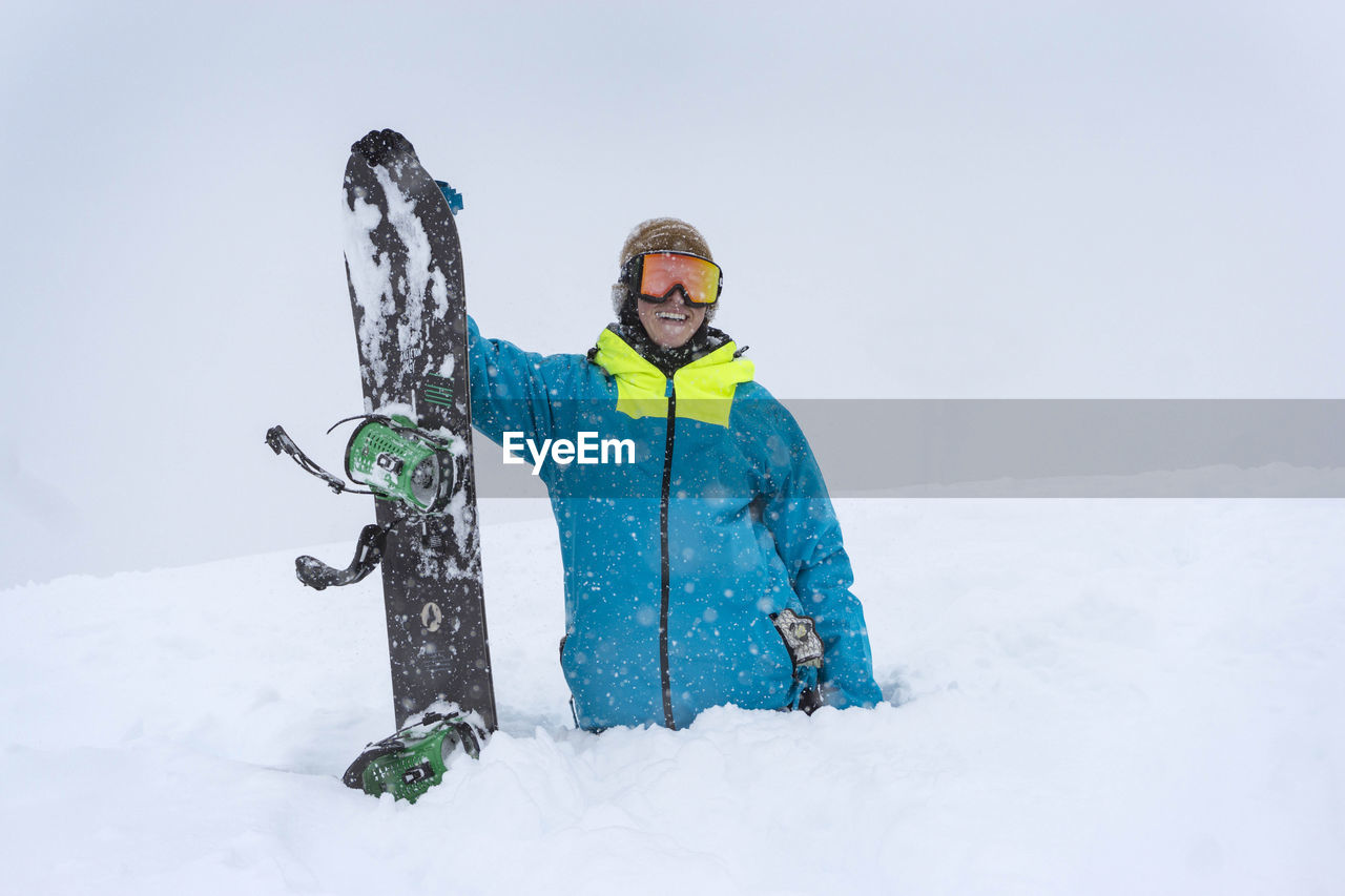 Happy male hiker with snowboard in deep powder snow