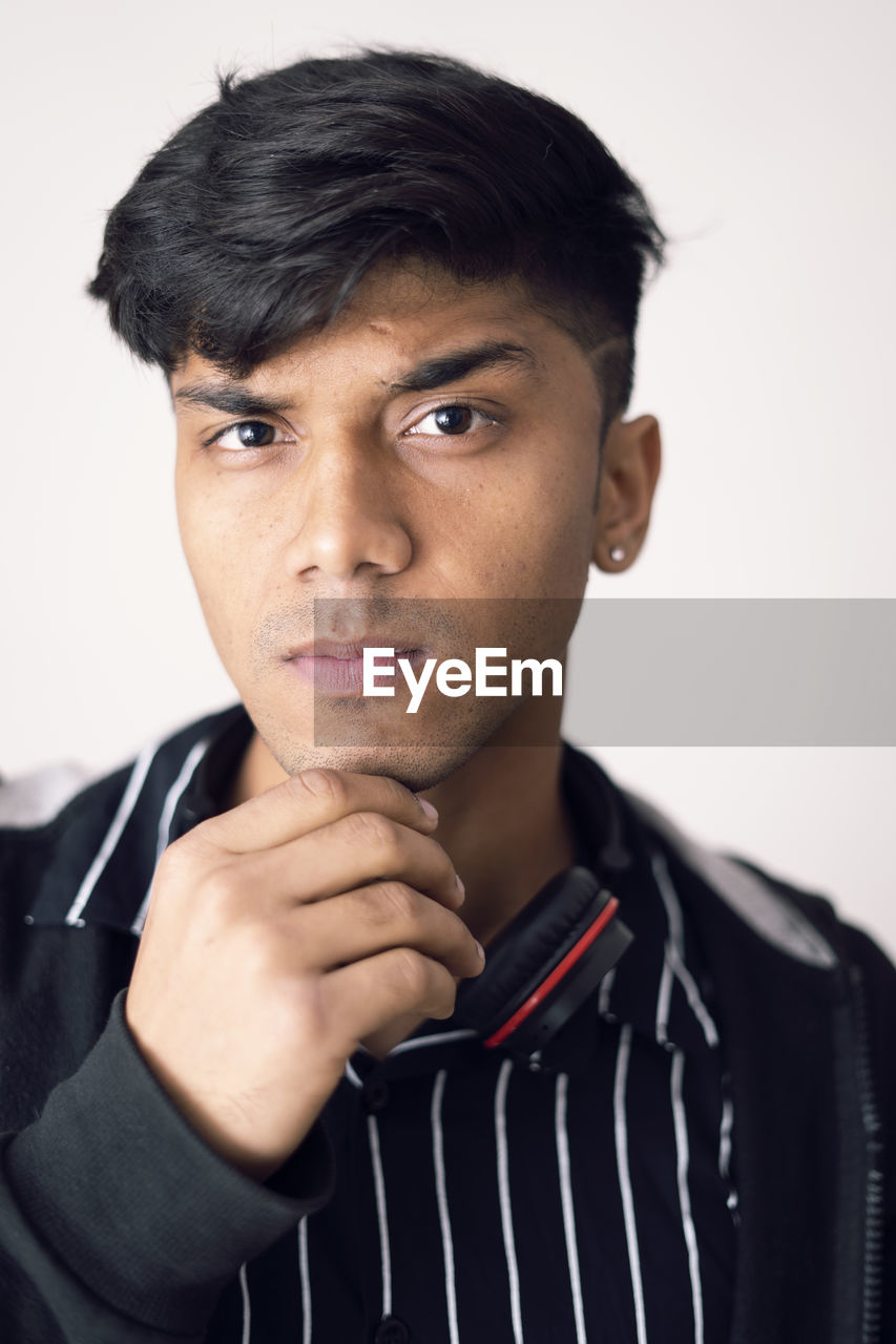 Portrait of young teenager resting chin on fist, clean shave and wearing black jacket.