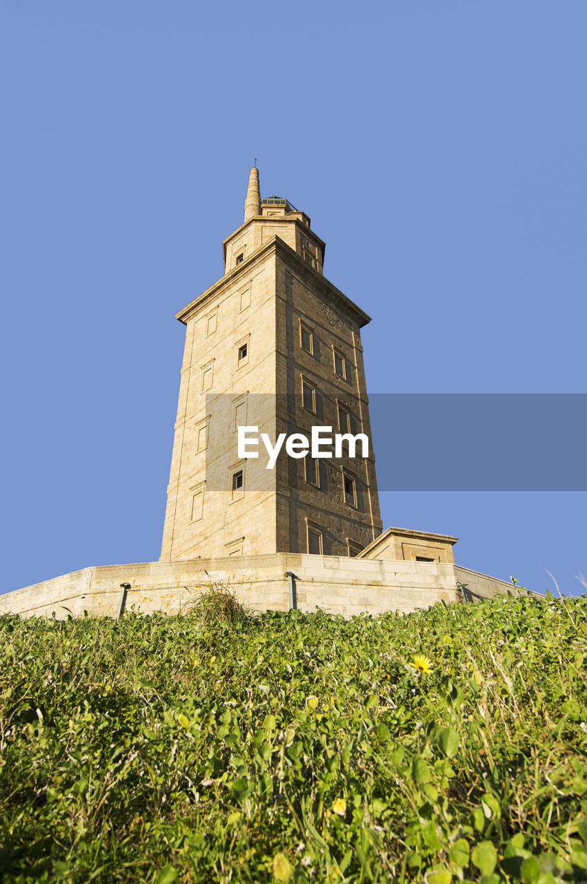 Tower of hercules on field against clear blue sky