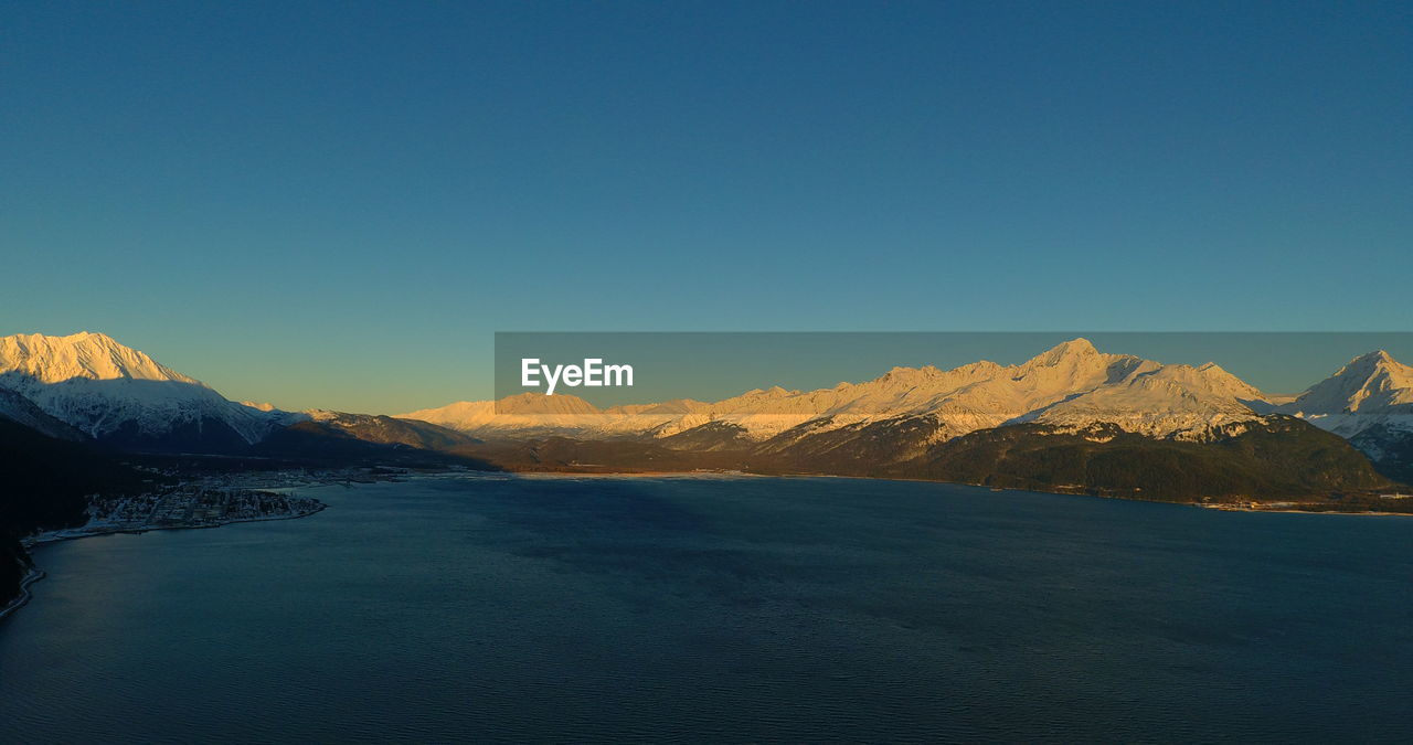 Scenic view of snowcapped mountains by sea against clear sky