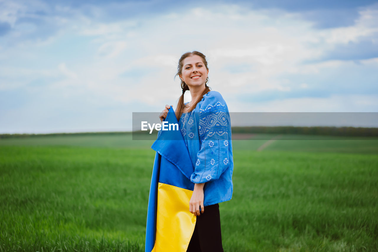 portrait of young woman standing on field against sky