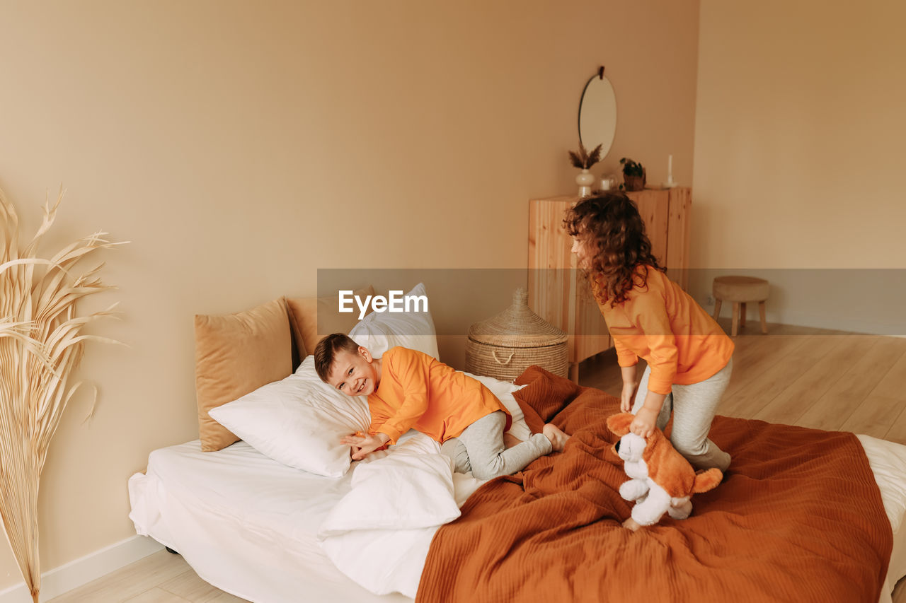 Funny happy kids brother and sister in pajamas playing having fun in a cozy bedroom at home