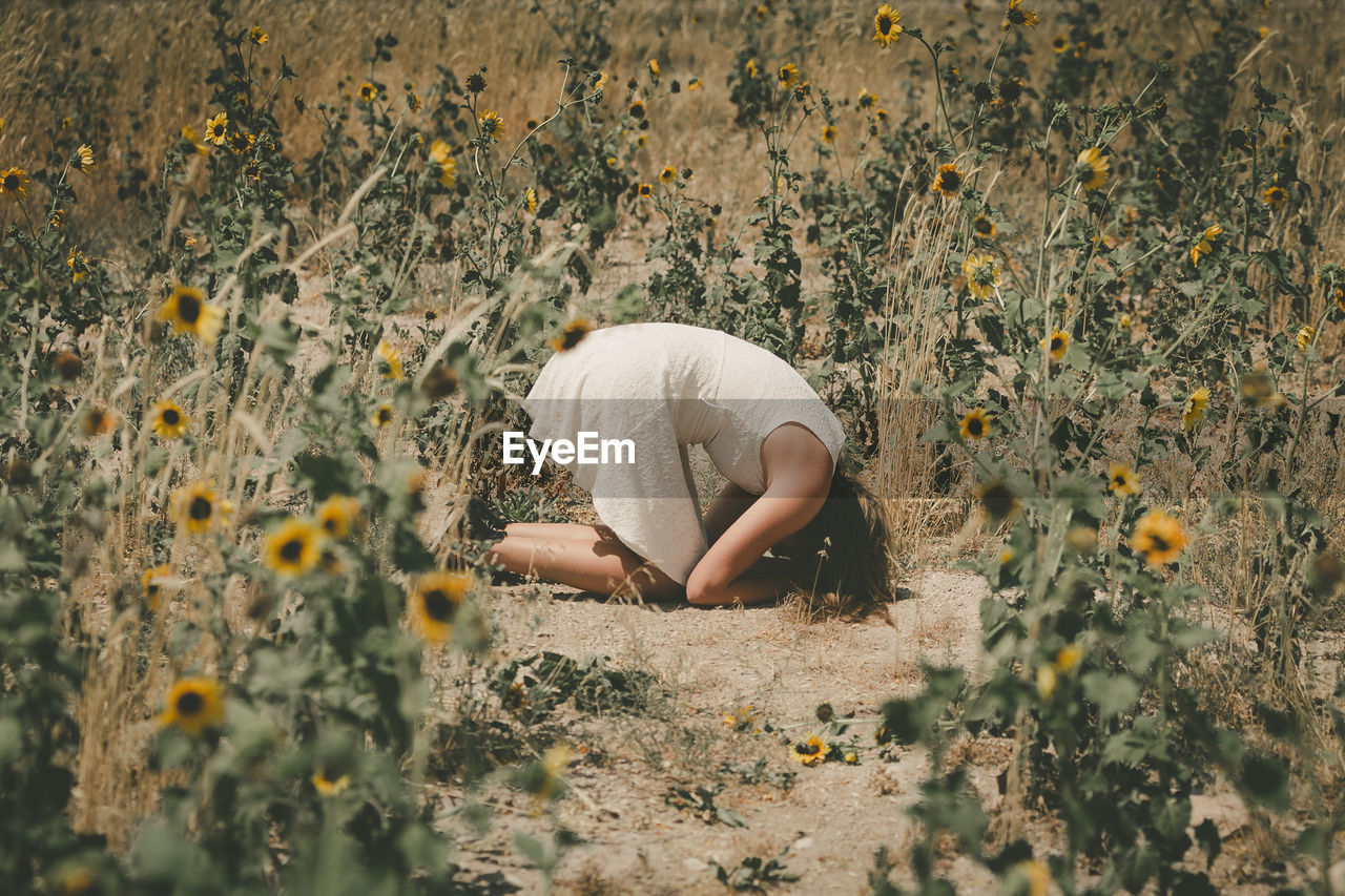 Side view of upset woman kneeling amidst plants on field