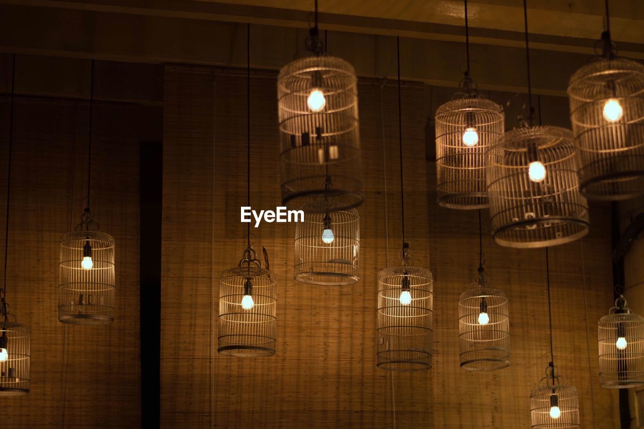 LOW ANGLE VIEW OF ILLUMINATED PENDANT LIGHTS HANGING IN CEILING