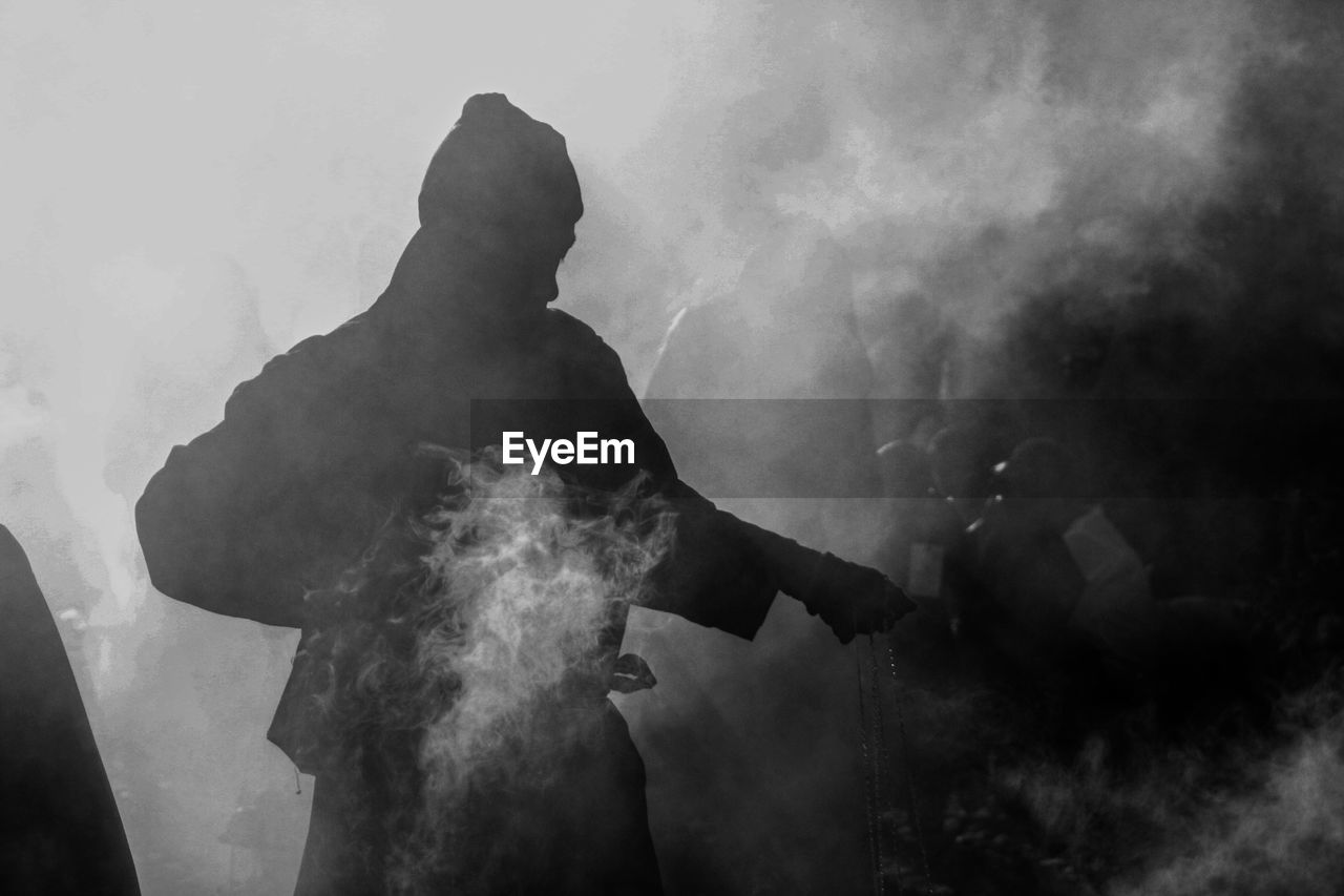 Smoke surrounded by man carrying incense burner