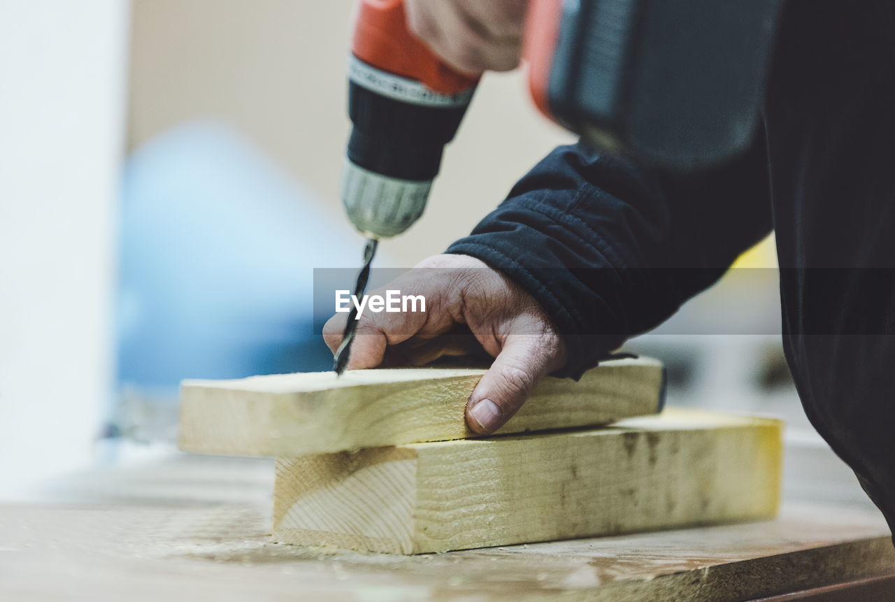 Midsection of carpenter drilling wood on table in workshop