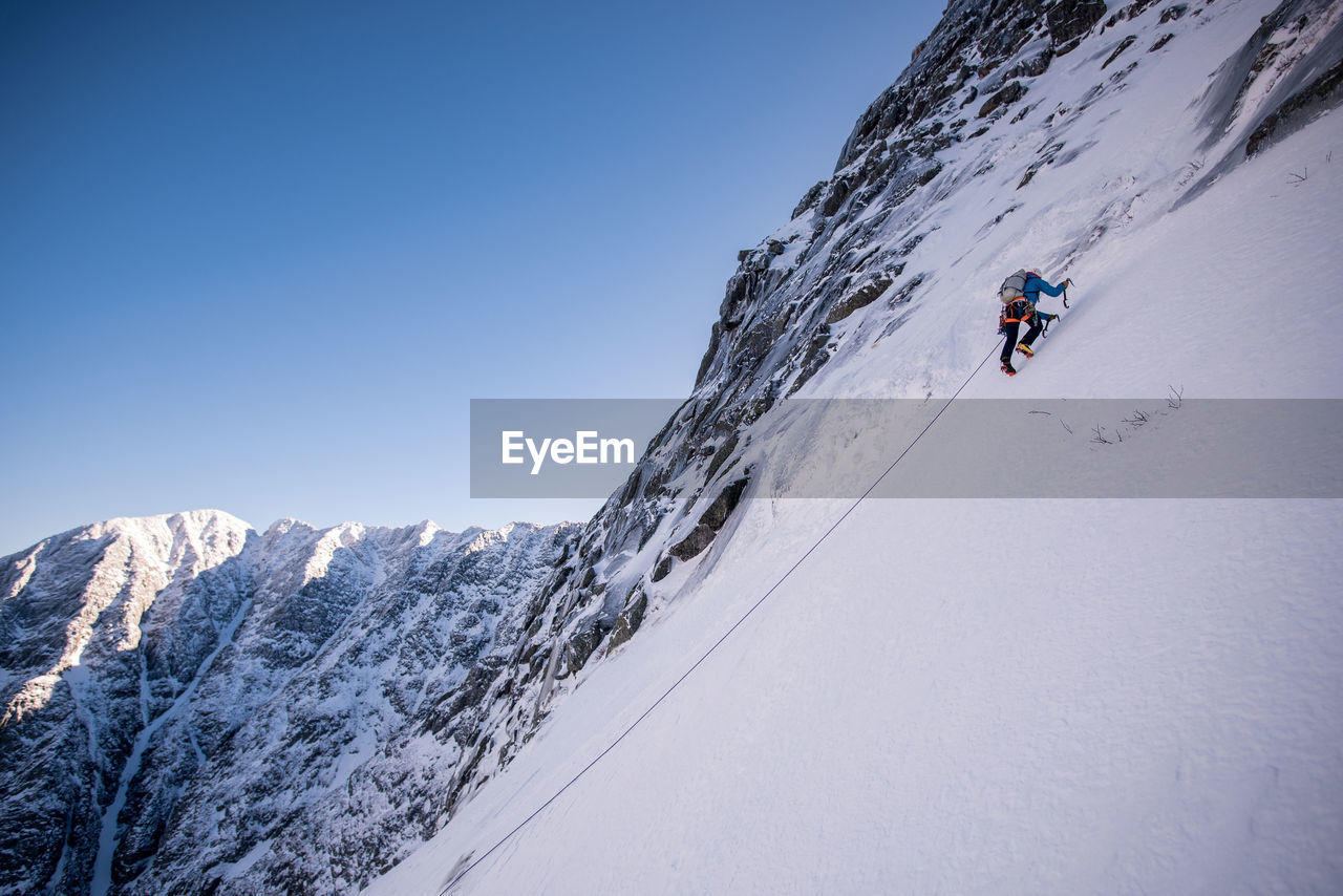 Alpine climber ascending steep snow with mountains behind