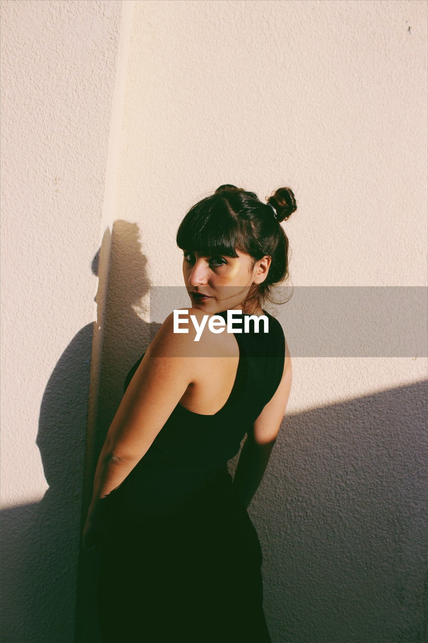 Rear view portrait of young woman standing against wall