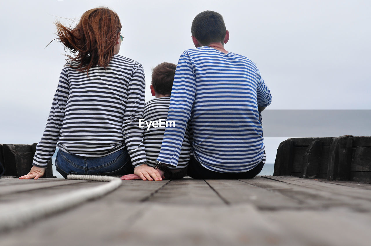 Rear view a family of three, dressed in blue striped longsleeve, holding hands, a child in between