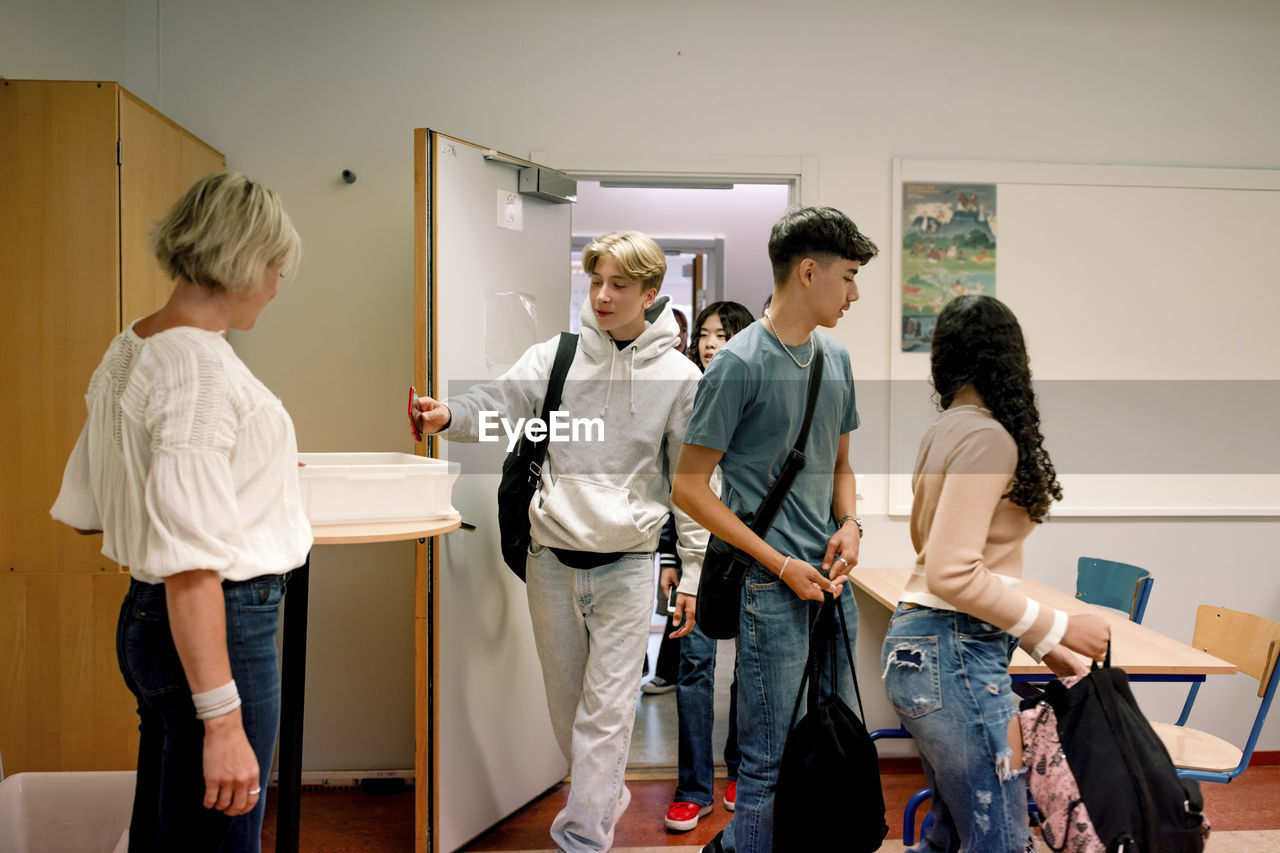 Teenage boy keeping smart phone in container on table while walking in classroom