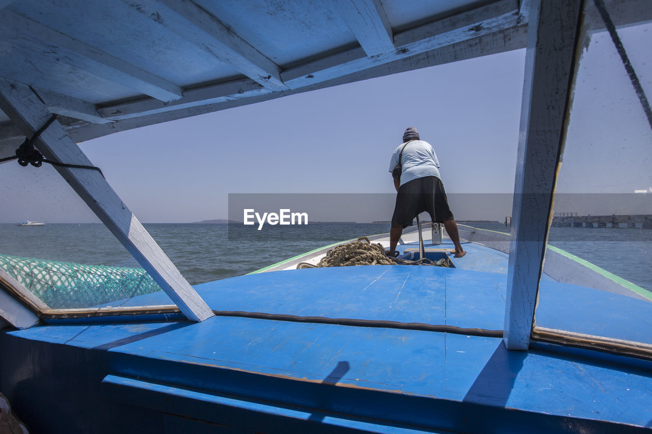 REAR VIEW OF MAN SITTING ON BOAT AT SEA