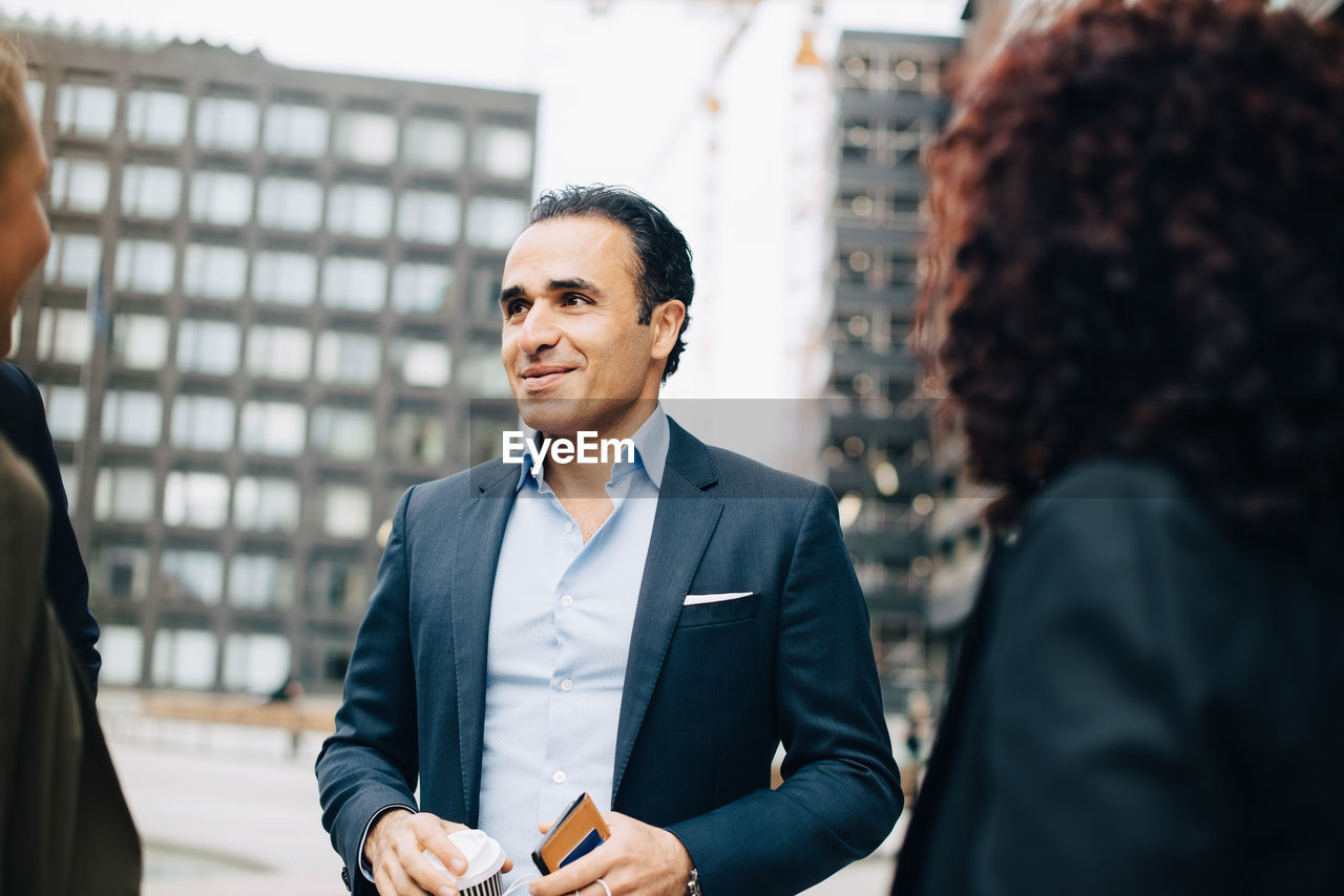 Smiling mature businessman talking with female colleagues in city