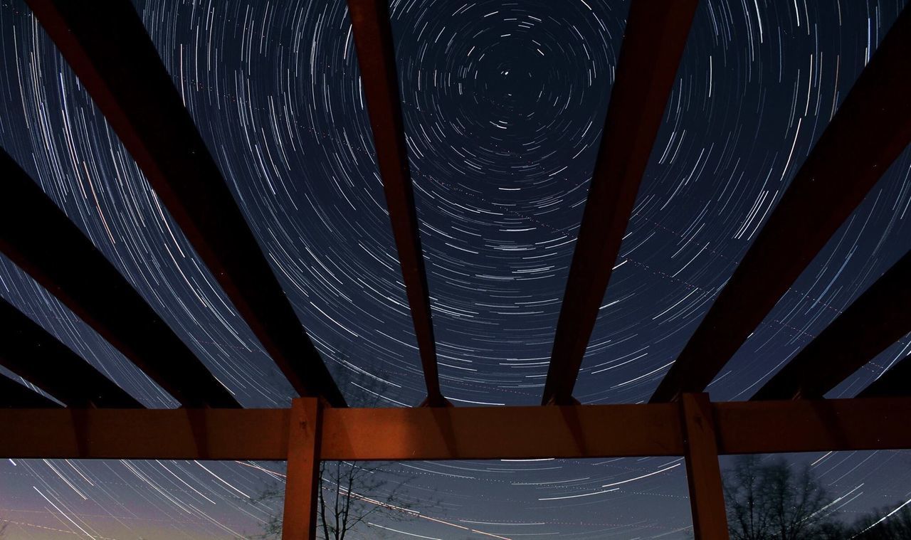 Low angle view of star trails seen through built structure at night