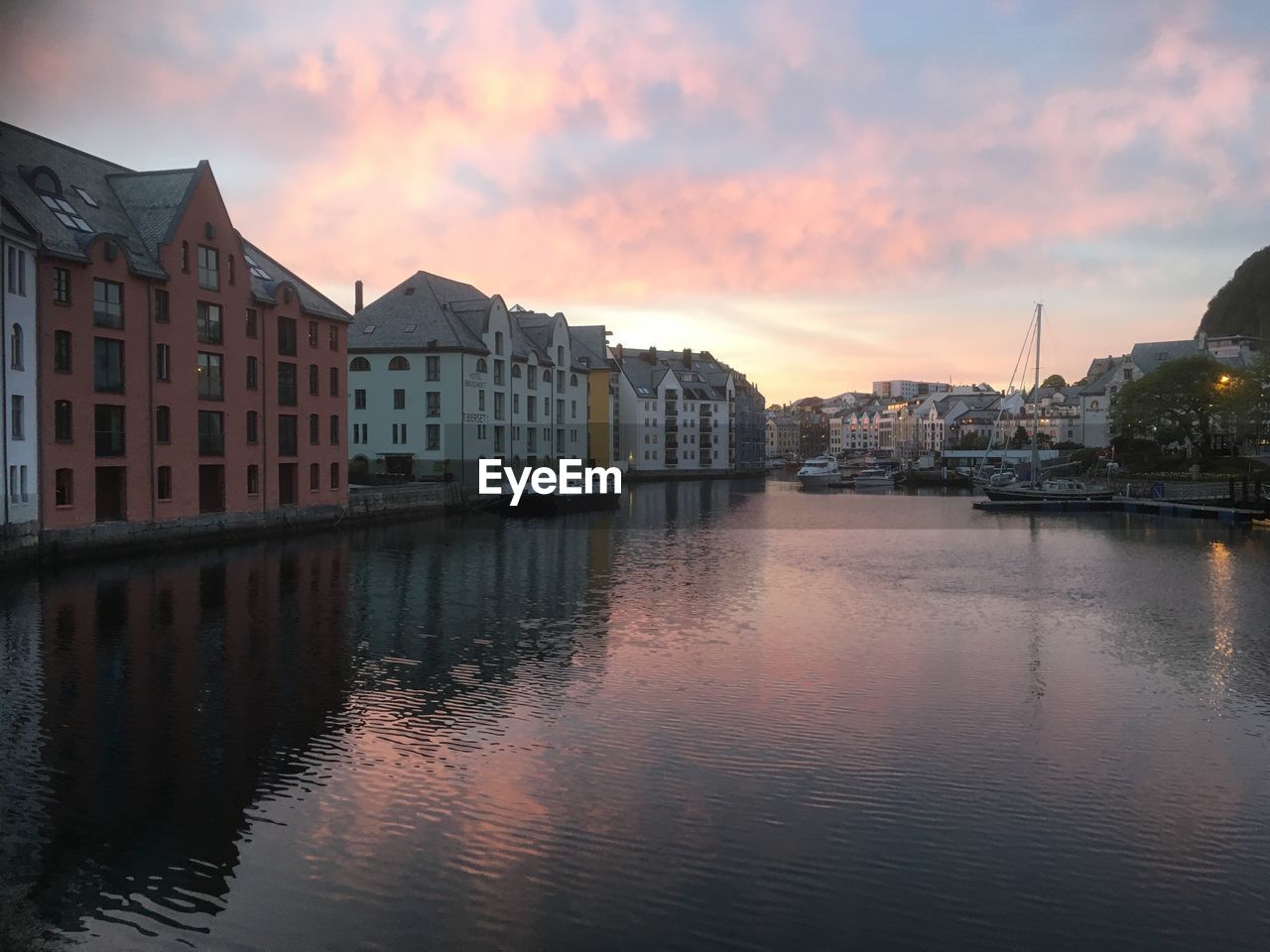 Buildings by river against sky during sunset