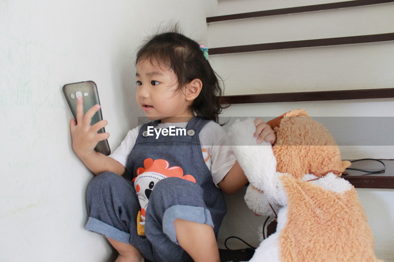 Cute baby girl playing phone cover while sitting on steps at home