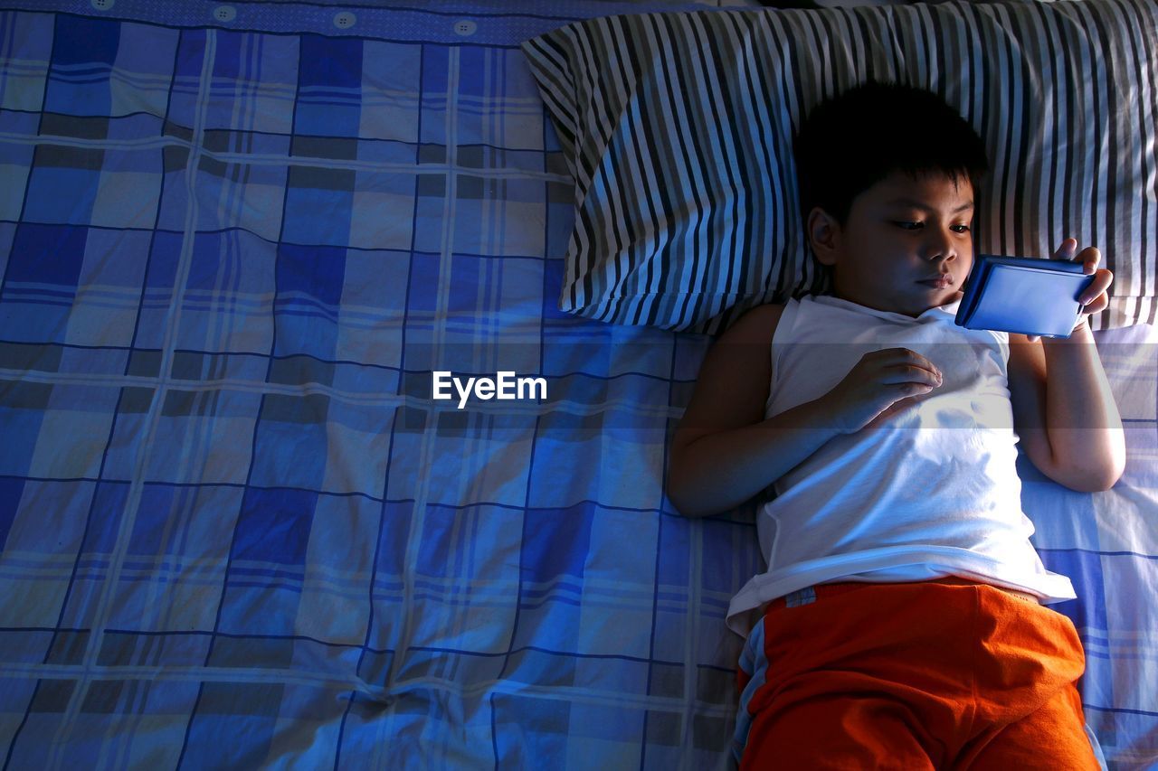 High angle view of boy using smart phone while lying down on bed at home