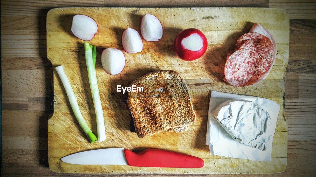 Directly above shot of bread with meat and vegetables on cutting board at table