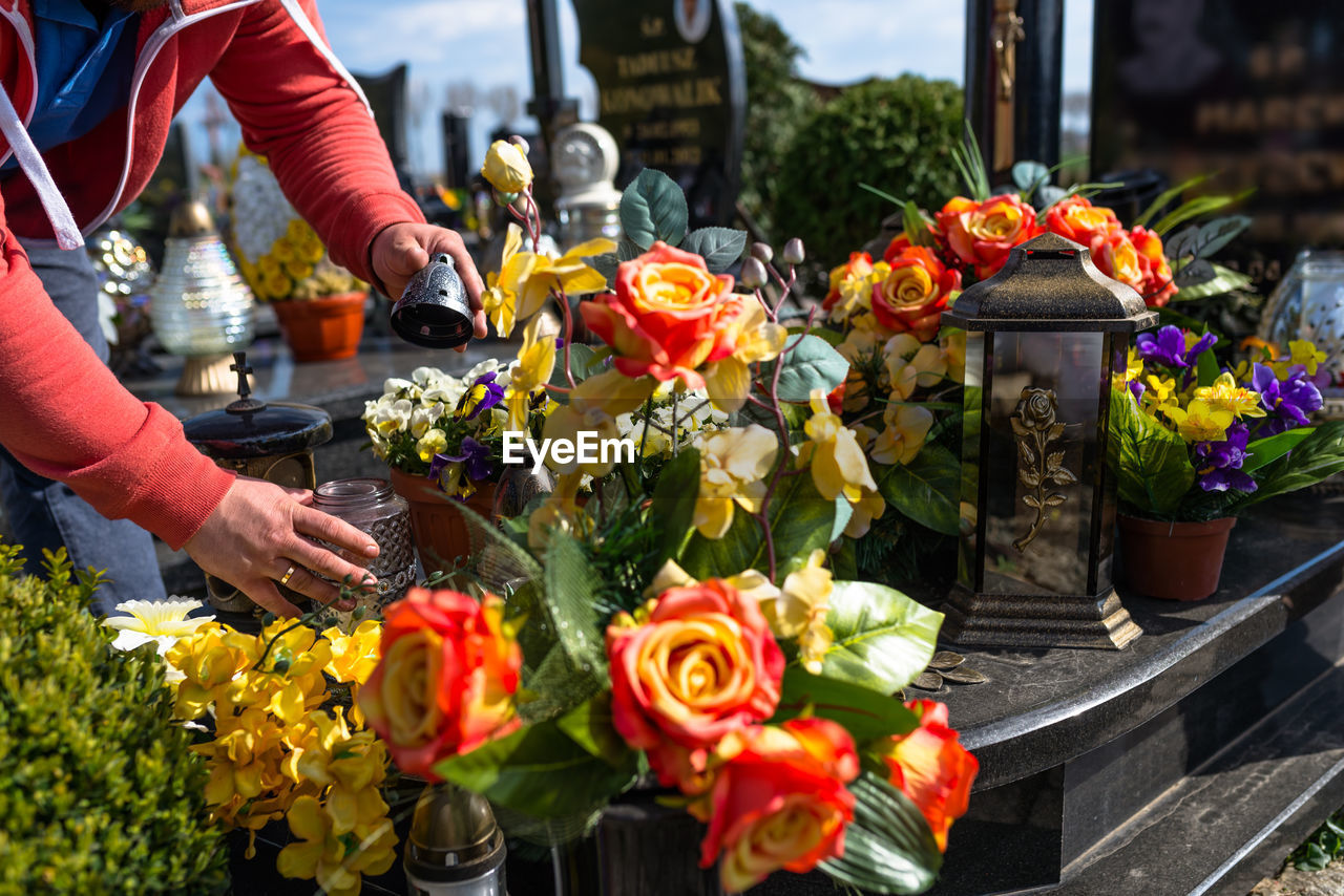 Artificial flowers and candlesticks lie on the tombstone in the cemetery, visible hands of a man.