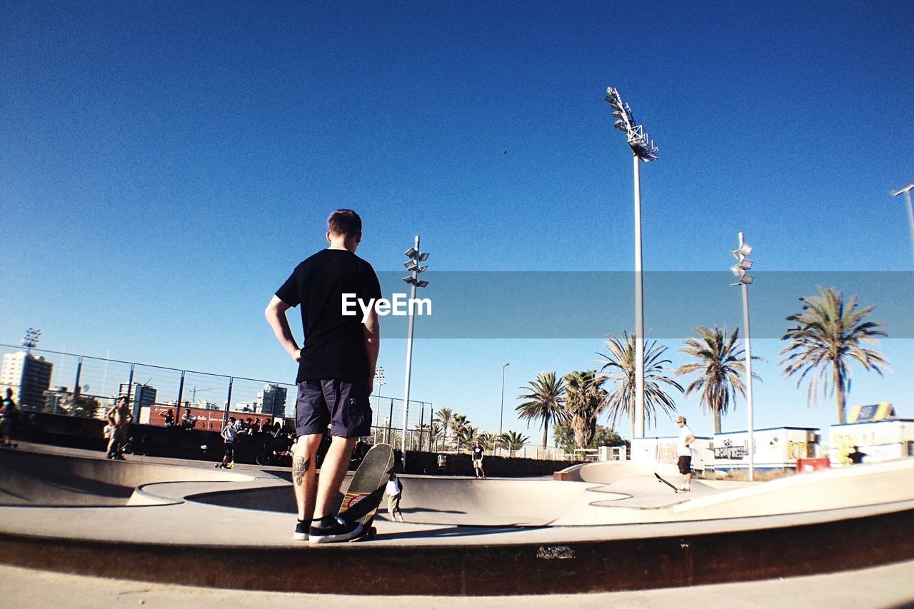 Rear view of skateboarder standing at skateboard park against clear sky