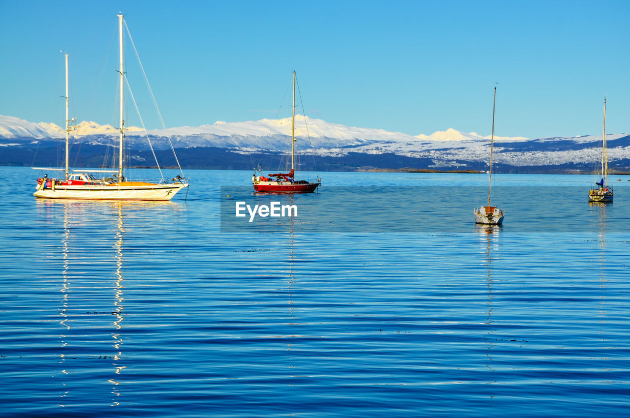 Boats on lake against snowcapped mountains
