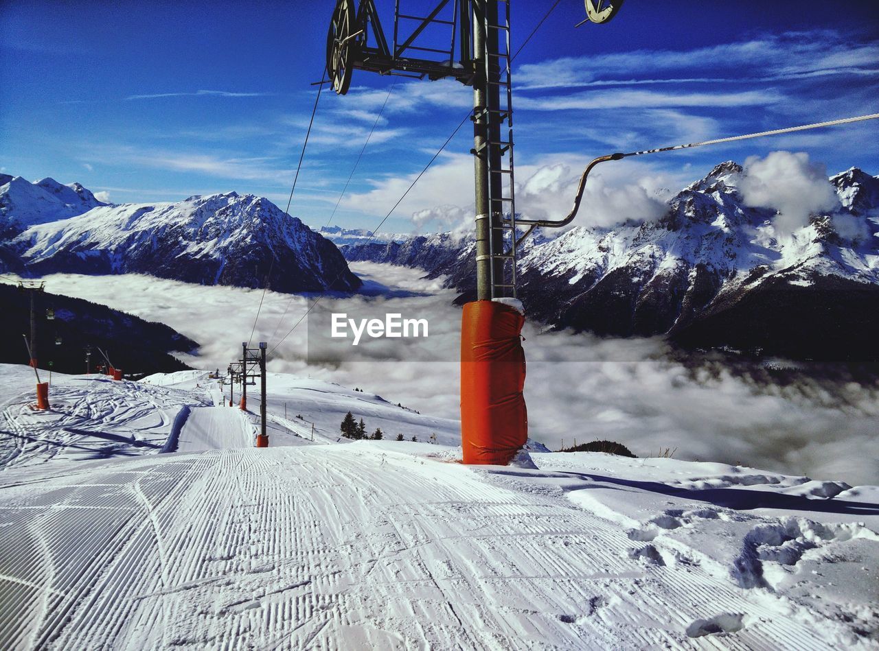 Ski lift poles on snow covered landscape by mountains against sky