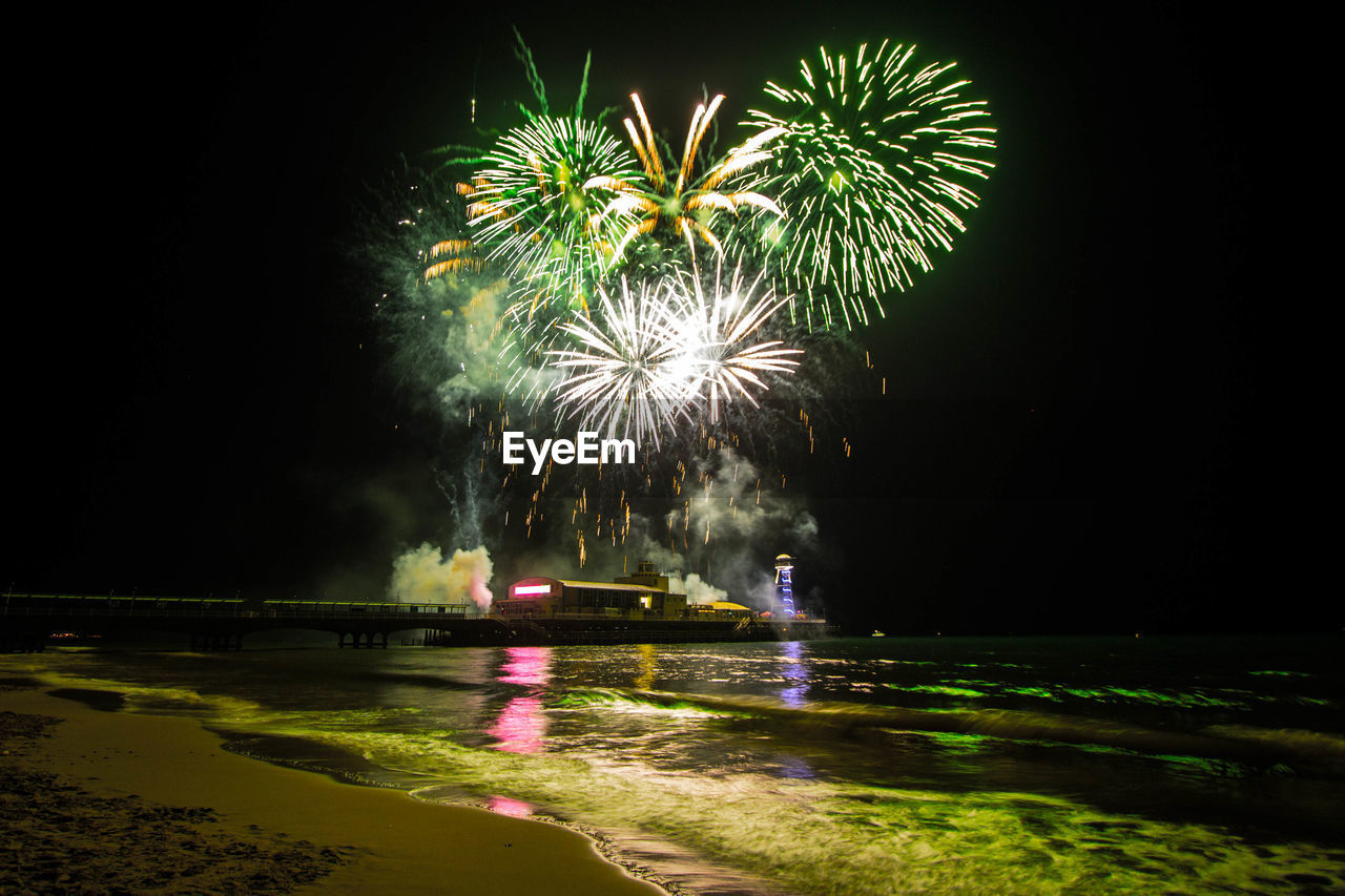 Firework display over sea against sky at night